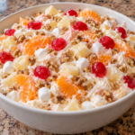 Ambrosia salad topped with maraschino cherries and chopped walnuts in a white serving bowl.